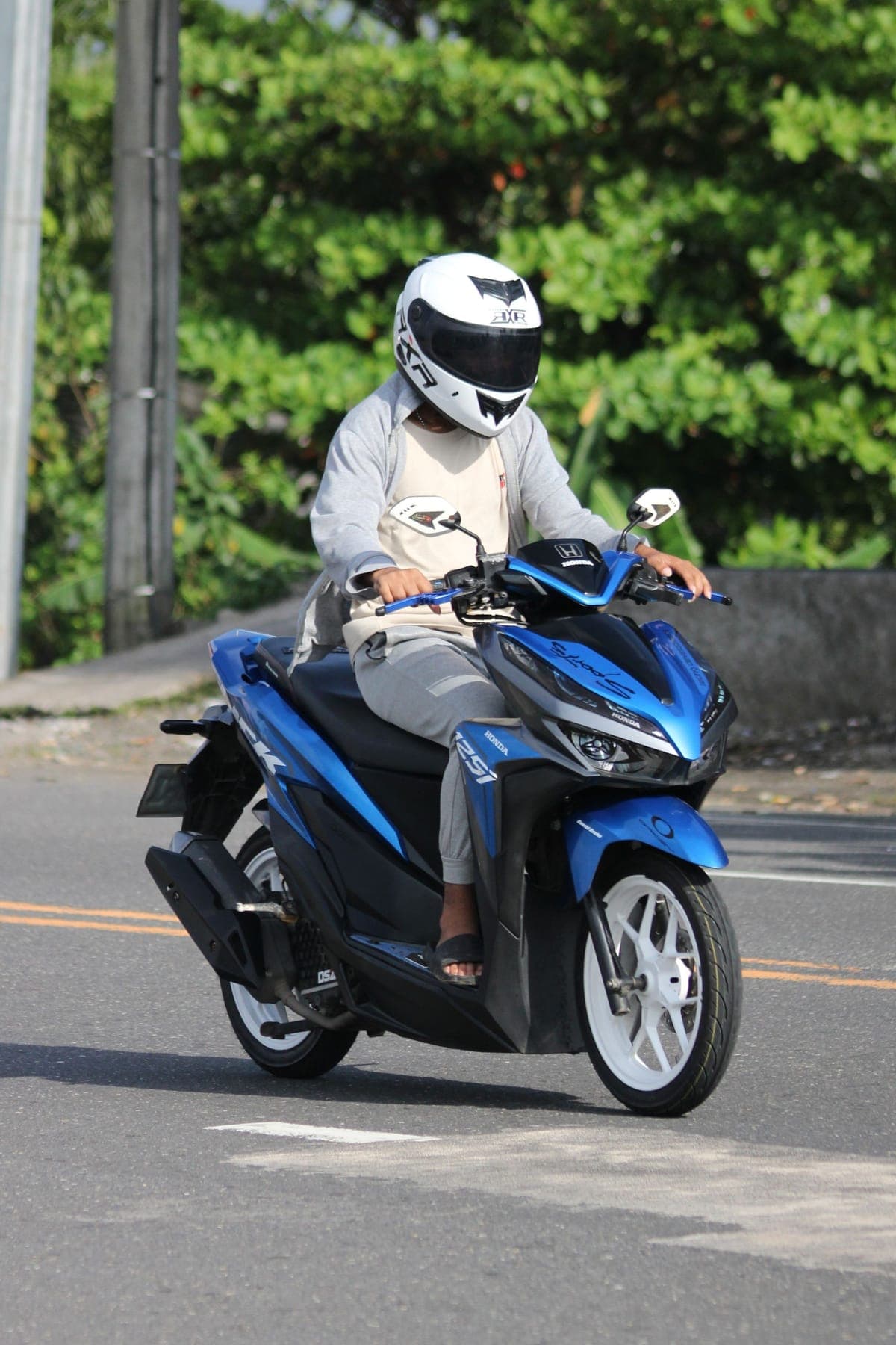 A rider in a white helmet on a scooter on a sunlit street